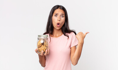 young hispanic woman looking astonished in disbelief and holding a cookies glass bottle