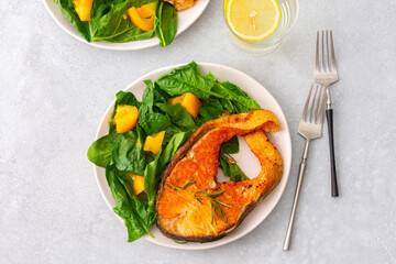 Fried salmon steak with spinach and yellow tomatoes in a plate on a gray background, a glass of...