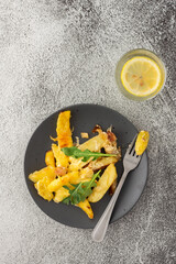 Stewed young potatoes with meat and cheese in a plate with arugula, lemon water in a glass, top view