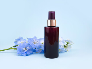 Fototapeta na wymiar Unbranded brown cosmetic spray bottle and blue Delphinium flower on blue background. Skincare beauty and liquid antibacterial spray concept. Natural organic spa Body mist. Mockup, closeup, front view.