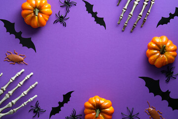 Halloween decorations on purple background. Happy Halloween concept. Flat lay pumpkins, bony hands, bats silhouettes, spiders.