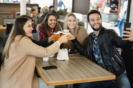 Group friends drinking beer while making selfie with mobile phone at brewery bar - Focus on man face