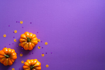 Happy Halloween concept. Flat lay orange pumpkins with confetti decorations on purple background. Top view with copy space.