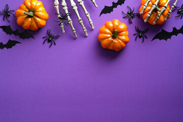 Halloween flat lay composition with pumpkins, bony hands, spiders, bats on purple background. Happy...