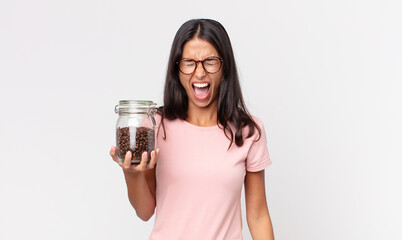 young hispanic woman shouting aggressively, looking very angry and holding a coffee beans bottle