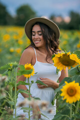 Portrait of a young beautiful woman with dark hair in a sunflower field at sunset. Happy. Summer.