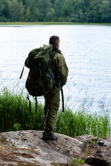 Young man travelling alone with a backpack. Concept of active tourism, camping in the forecast, trekking and hiking during vacations. Green background. Copy space for text