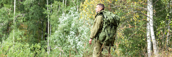 Young man travelling alone with a backpack. Concept of active tourism, camping in the forecast, trekking and hiking during vacations. Green background. Copy space for text banner