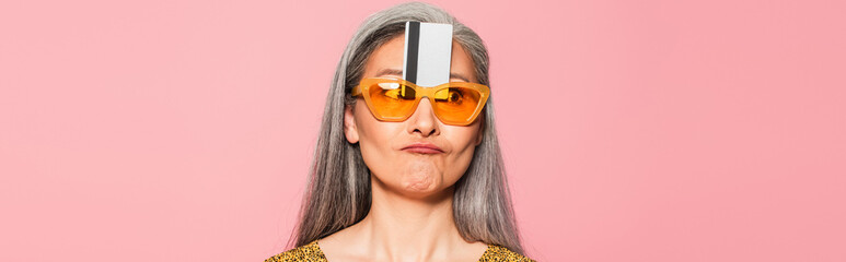 mature woman in yellow sunglasses with credit card near forehead isolated on oink, banner