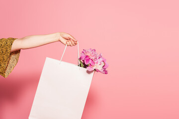 partial view of woman with fresh peonies in shopping bag on pink background