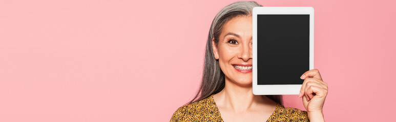 happy mature woman obscuring face with digital tablet isolated on pink, banner