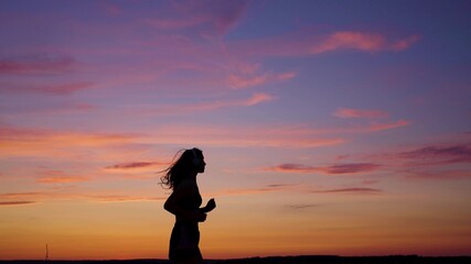 Silhouette of free young woman runs in summer in park at sunset, listens to music on headphones. Training jogging. Healthy jogging and outdoor exercise. Listen to music without Internet, play sports