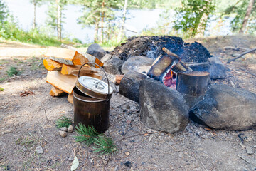 Metal bowler pot near bonfire and stake of wood. Preparation of soup or tea. Concept of traveling,...