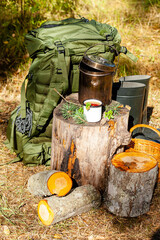 Backpack of traveller, bowler pot, enameled mug with coffee or tea, on wooden stump in the forest....