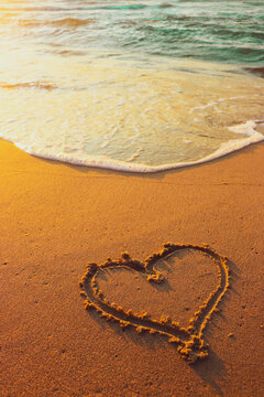 A heart drawing in the sand. Ocean waves on the beach. Happy holiday concept. Vertical background photo