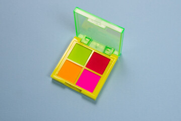 Purple, green, orange and blue eye shadow palette isolated on a blue background. Make up. Neon colours.