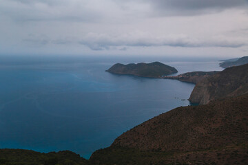 Fototapeta premium Top view at Asos village and Assos peninsula during bad weather conditions, thunderstorm and rain, with low dark clouds and visible currents at sea. Cephalonia, Greece.