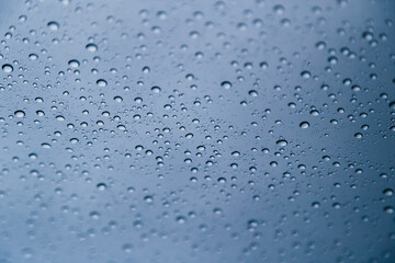 Close up of rain drops on window with blue gray background of dark sky