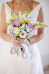Sposa in abito bianco che regge fra le mani un bouquet di fiori di campo colorati