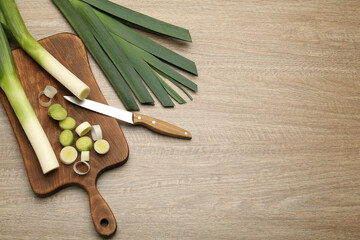 Fototapeta na wymiar Fresh raw leeks and knife on wooden table, flat lay. Space for text