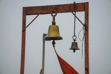 Stock photo of two ancient copper or bronze bell hanging on a orange color iron frame at hindu temple on blur foggy background. Picture captured at sateri hill station Kolhapur ,Maharashtra, India.