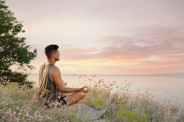 Man meditating in meadow near river. Space for text