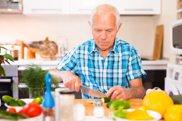senor man preparing fresh vegetable salad at home in the kitchen