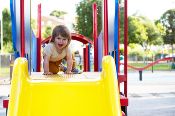 Happy toddler, baby or child on playground area. Playing kid at yellow plastic slidea. Education, active games outside.