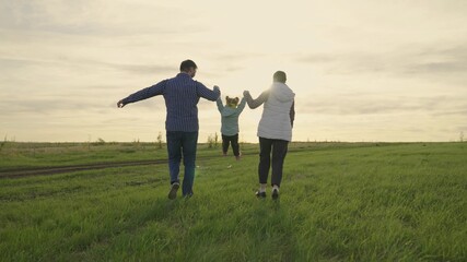 Mom, dad are a child, a daughter is running on the green grass, playing on the field. Happy family walks in the park holding hands in the summer at sunset. Teamwork. Happy healthy childhood