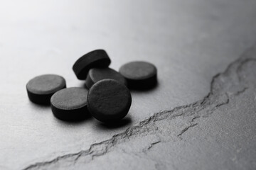 Fototapeta na wymiar Activated charcoal pills on black table, space for text. Potent sorbent
