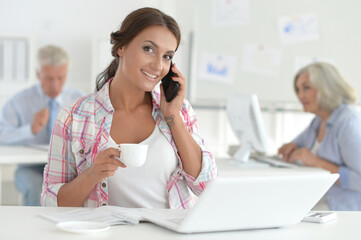 Beautiful young woman with smartphone working in office, colleagues on bckground