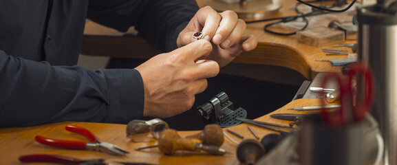 Close-up of goldsmith hand decorating precious ring with beautiful diamonds. Professional jeweler...