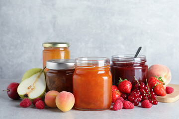 Fototapeta na wymiar Jars with different jams and fresh fruits on grey table