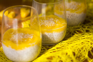 Chia pudding or smoothie with mango puree, coconut milc and coconut chips in transparent glasses  