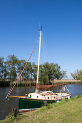 Traditional green wooden sailing boat with mast moored on riverbank