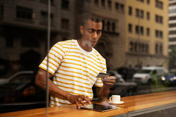 Fototapeta na wymiar Handsome young african man in cafe drinking coffee. Portrait of happy man with credit card drinking coffee in cafe..
