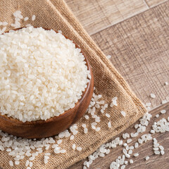 Raw white rice in a wooden bowl over table.