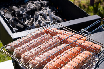Raw sausages on grill on the charcoal grill, summer picnic in nature, barbecue bbq grill traditional German bratwurst hot dogs 