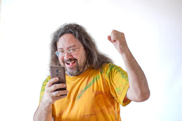 The man happily looks at the phone. A casually and sloppy dressed man with a beard and long hair in...