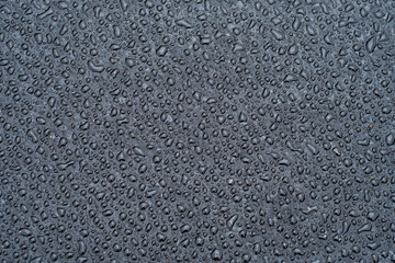 Dark background with large water droplets on newly paved asphalt. Road surface wet from rain after repair work.
