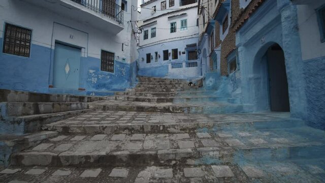 Forwards reveal of stairs between blue painted houses in Chefchaouen. Low angle view. Morocco, Africa