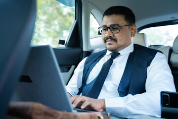 Businessman working on laptop while travelling in car - concept of successful business, modern lifestyle, internet, technology and communication