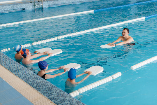 A group of boys and girls train and learn to swim in the pool with an instructor. Development of children's sports.