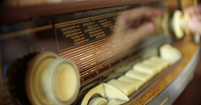 Close-up of a hand turning on a vintage Soviet radiola. nostalgic shot of a hand using an analog radio. soft-lit display of a vintage radio. cinematic closeup of reflected in the radiola hand catching