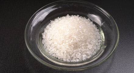 Sugar in glass bowl on wooden background.