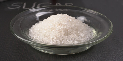 Sugar in glass bowl on wooden background.
