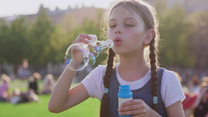 Medium shot of preteen girl blowing soap bubbles in summer park