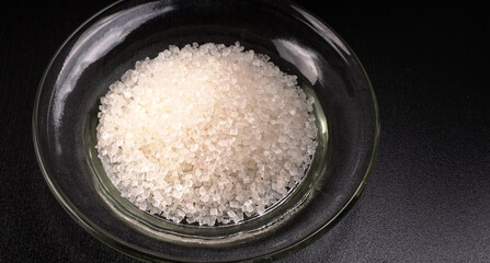 Sugar in glass bowl on wooden background.