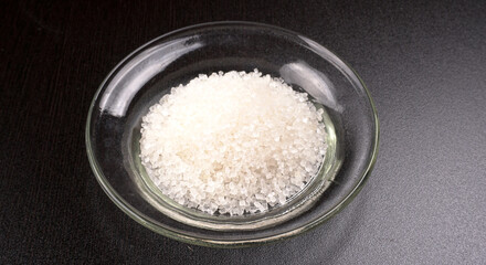 Sugar in glass bowl on wooden background.