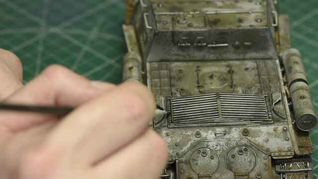 Scale Modeling. A man makes mud weathering on a WWII plastic model of a tank. Close up painting on 1:35 scale model. Plastic Modeling and model building. Hobby and leisure at home. 